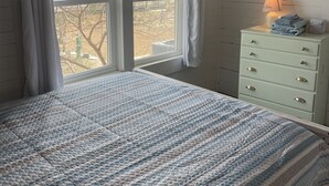Une chambre à coucher avec un lit, une commode, une lampe et une fenêtre avec des rideaux.