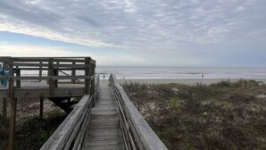Une promenade en bois menant à une plage, avec un ciel nuageux.