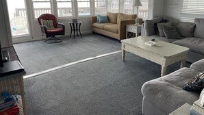 Un salon chaleureux avec un canapé beige, un fauteuil rouge, une table basse blanche et une petite table ronde.