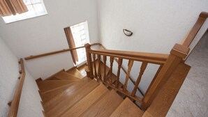 A wooden staircase with a handrail, a small window with curtains, and a wall-mounted light fixture. - APARTMAN MIKELIN(2+1) AND 2 ROOMS(EACH FOR 2 PEOPLE) (Primošten)
