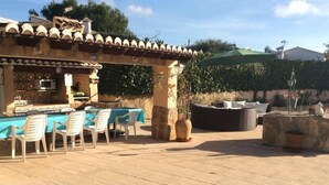 Eine Terrassengruppe mit Tisch, Stühlen, einem großen Pflanzkübel und einer Pergola mit grünem Sonnenschirm.