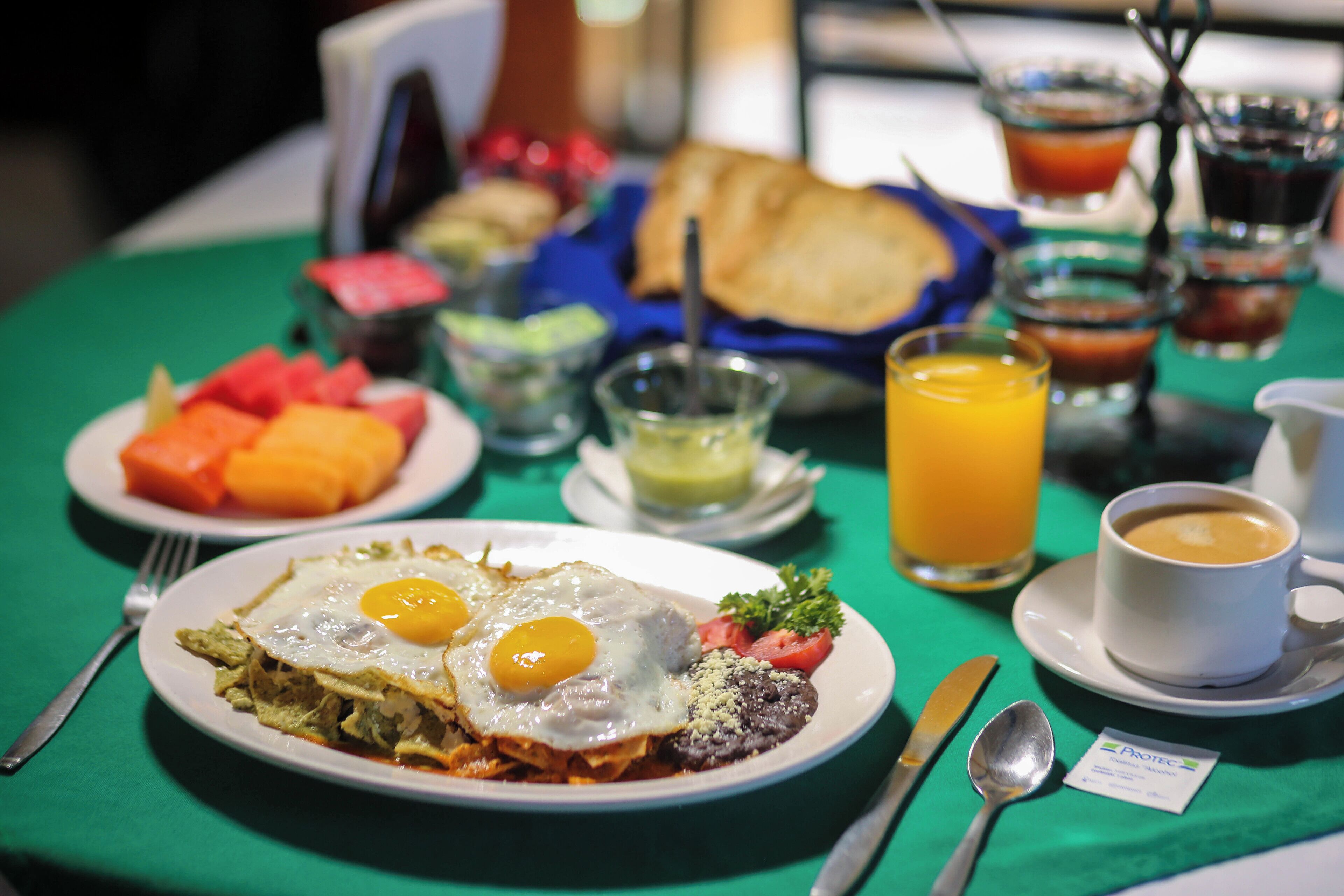 Un desayuno con platos de comida, incluyendo huevos, vegetales y tostadas, además de una taza de café y un vaso de jugo de naranja.
