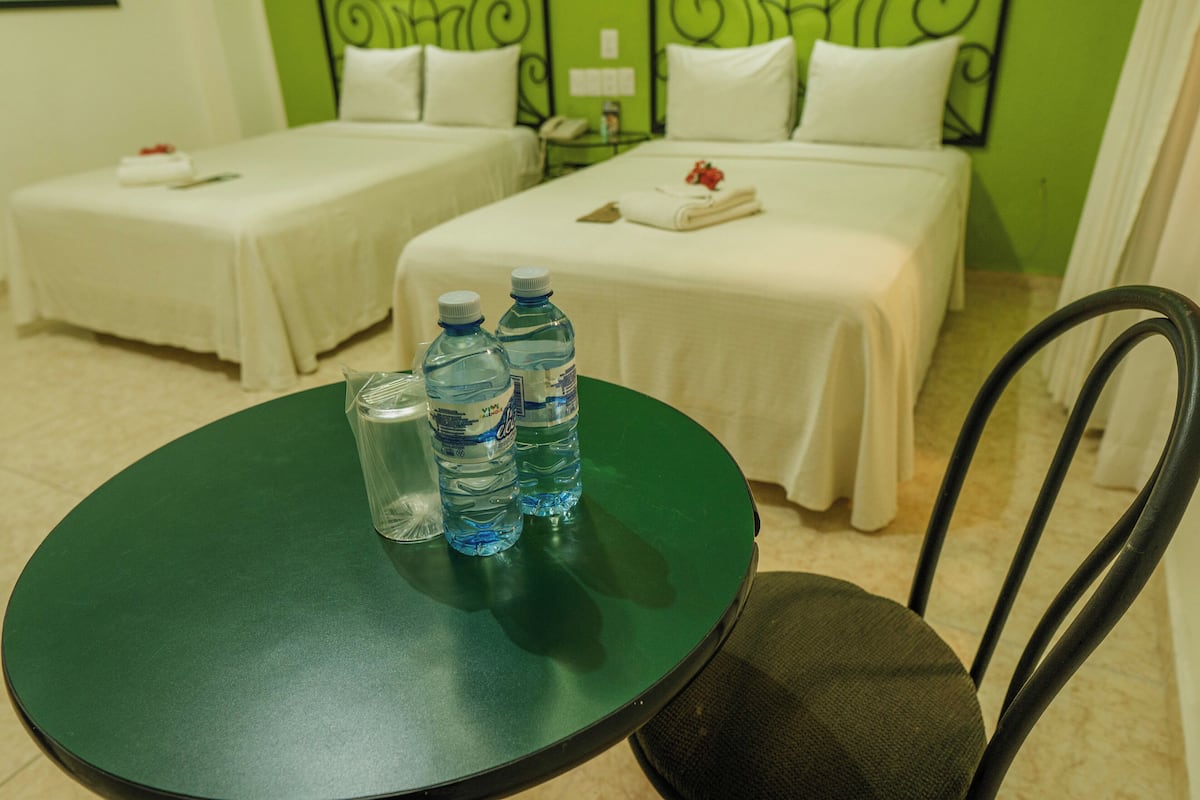 Habitación de hotel con dos camas, una mesa verde con botellas de agua y una silla.