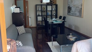 Una sala de estar moderna con un sofá, una mesa de comedor para dos personas, una estantería y un cuadro abstracto de gran tamaño.