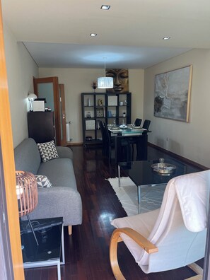 A modern living room with a sofa, a dining table set for two, a bookshelf, and a large abstract painting.