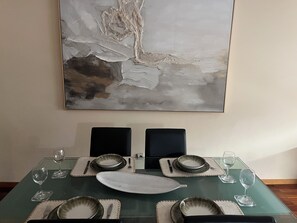 Mesa de jantar posta com pratos, copos e talheres, com uma pintura abstrata moderna acima.