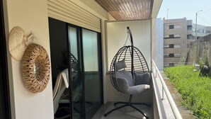 Un balcón con una hamaca colgante, un adorno de pared tejido y vistas a un edificio y vegetación.