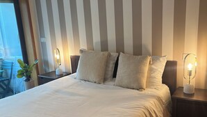 Una cama bien hecha con cubrecama blanco, dos mesitas de noche con lámparas y una pared a rayas.