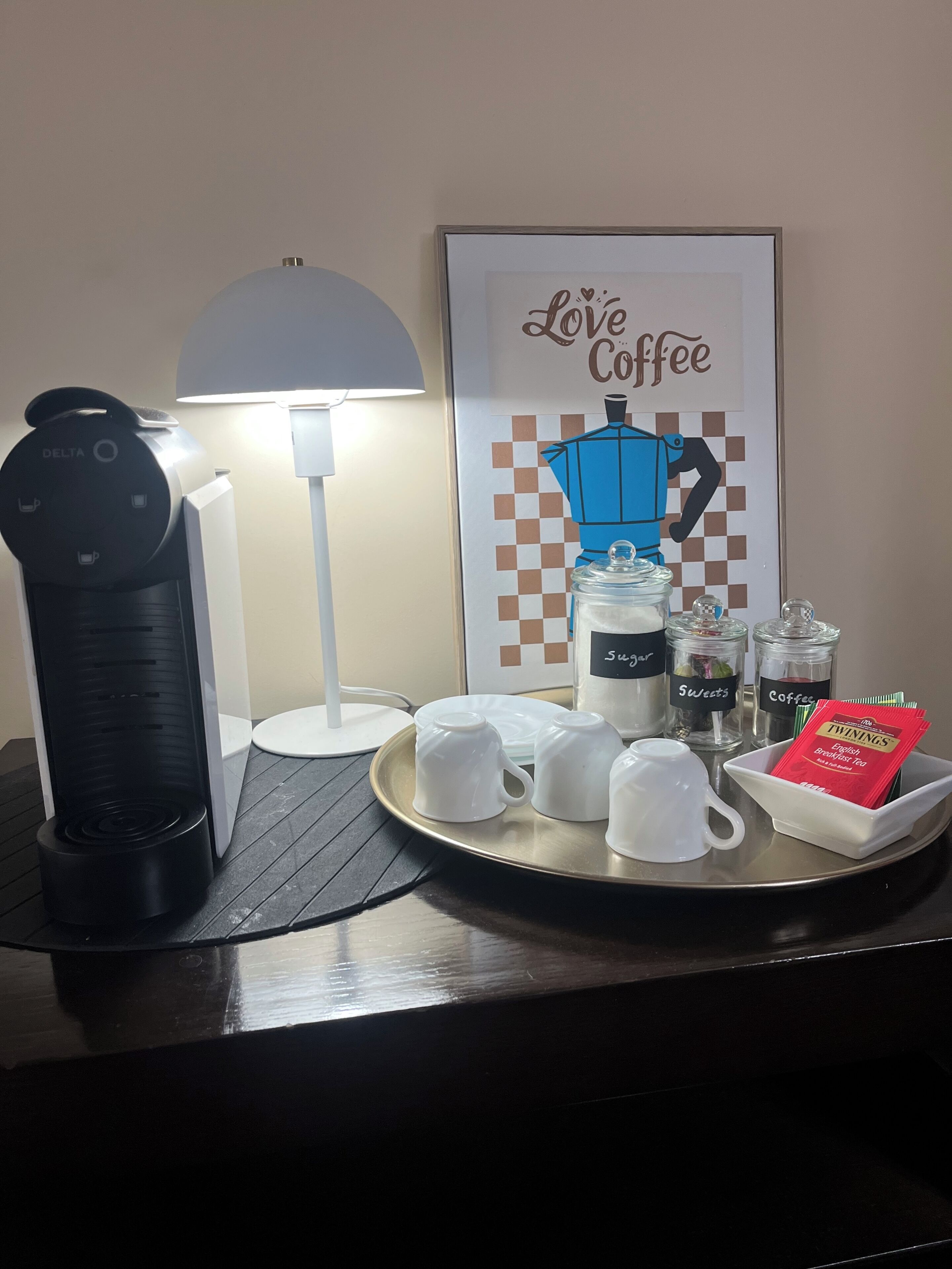A coffee station with a coffee maker, cups, sugar and coffee containers, and a tray with tea packets.