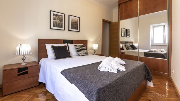 A hotel room with a large bed, two bedside tables, a mirror, and two framed pictures on the wall. - Casa Campolide - Lisbon (Lisboa)