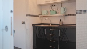 Una cocina compacta con encimera negra, salpicadero blanco de azulejos y un estante sobre el lavamanos.