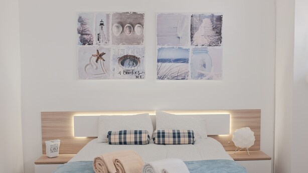 Una cama bien hecha con funda azul, dos toallas enrolladas y una mesita de noche con lámpara y un adorno.