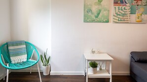 Una habitación con una silla turquesa, una mesita blanca y una planta de cactus.
