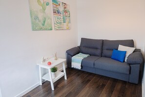 Un salon avec un canapé gris, une table d’appoint blanche et deux œuvres d’art murales.