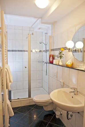 Un baño con cabina de ducha de vidrio, inodoro y lavamanos con espejo.