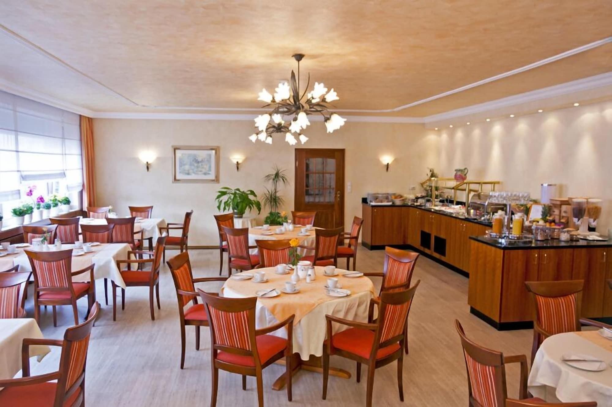 Ein Hotel-Essbereich mit mehreren Tischen, Stühlen, einer Speiseauslage und einer Kronleuchter.