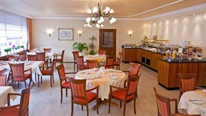 A hotel dining area with multiple tables and chairs, a buffet counter, and a chandelier. - Rosenhof (Kerpen)