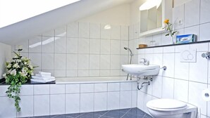 A modern bathroom with a bathtub, sink, and toilet. There is a mirror above the sink and a flower arrangement on the left. - Rosenhof (Kerpen)