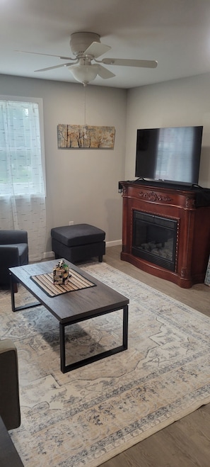 A living room with a fireplace, a ceiling fan, a flat-screen TV, and a coffee table. - Tin Brook Bed & Breakfast (Walden)