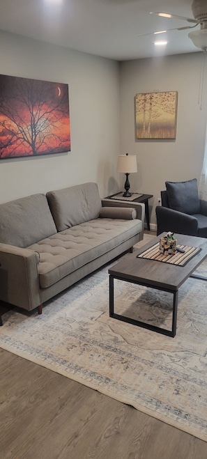 A living room with a sofa, coffee table, lamp, and artwork on the walls. - Tin Brook Bed & Breakfast (Walden)