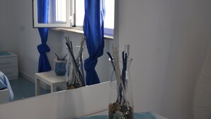 Et badeværelse med et spejl, et vindue med blå gardiner, en vask og en vase med pynteting.