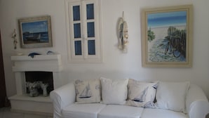 Un salon blanc avec un canapé blanc, une cheminée et trois tableaux accrochés au mur.