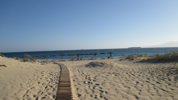 Une plage de sable avec une promenade en bois menant à des parasols de plage.