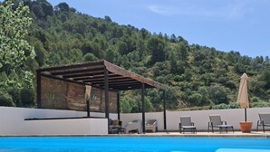 Ein klares, blaues Schwimmbecken mit einer Pergola und Liegestühlen, umgeben von einem üppigen, grünen Hügelhang.