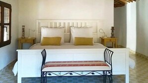 Ein Schlafzimmer mit Holzboden, einem weißen Bett mit zwei Kissen, einem Nachttisch und einem Sessel.