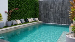 A swimming pool with a waterfall feature, a green wall, and a seating area with cushions. - Tamarindo 2 BR, 2 BA  (tamarindo)