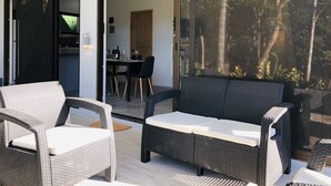 A modern outdoor seating area with wicker furniture, a dining table, and a view of a forest through large glass doors. - Tamarindo 2 BR, 2 BA  (tamarindo)