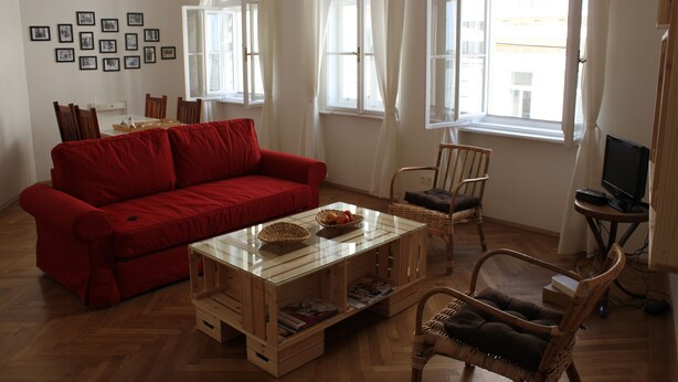 Ein Wohnzimmer mit einem roten Sofa, einem Couchtisch aus Glas, Korbstühlen und einem Fernseher auf einem Lowboard.