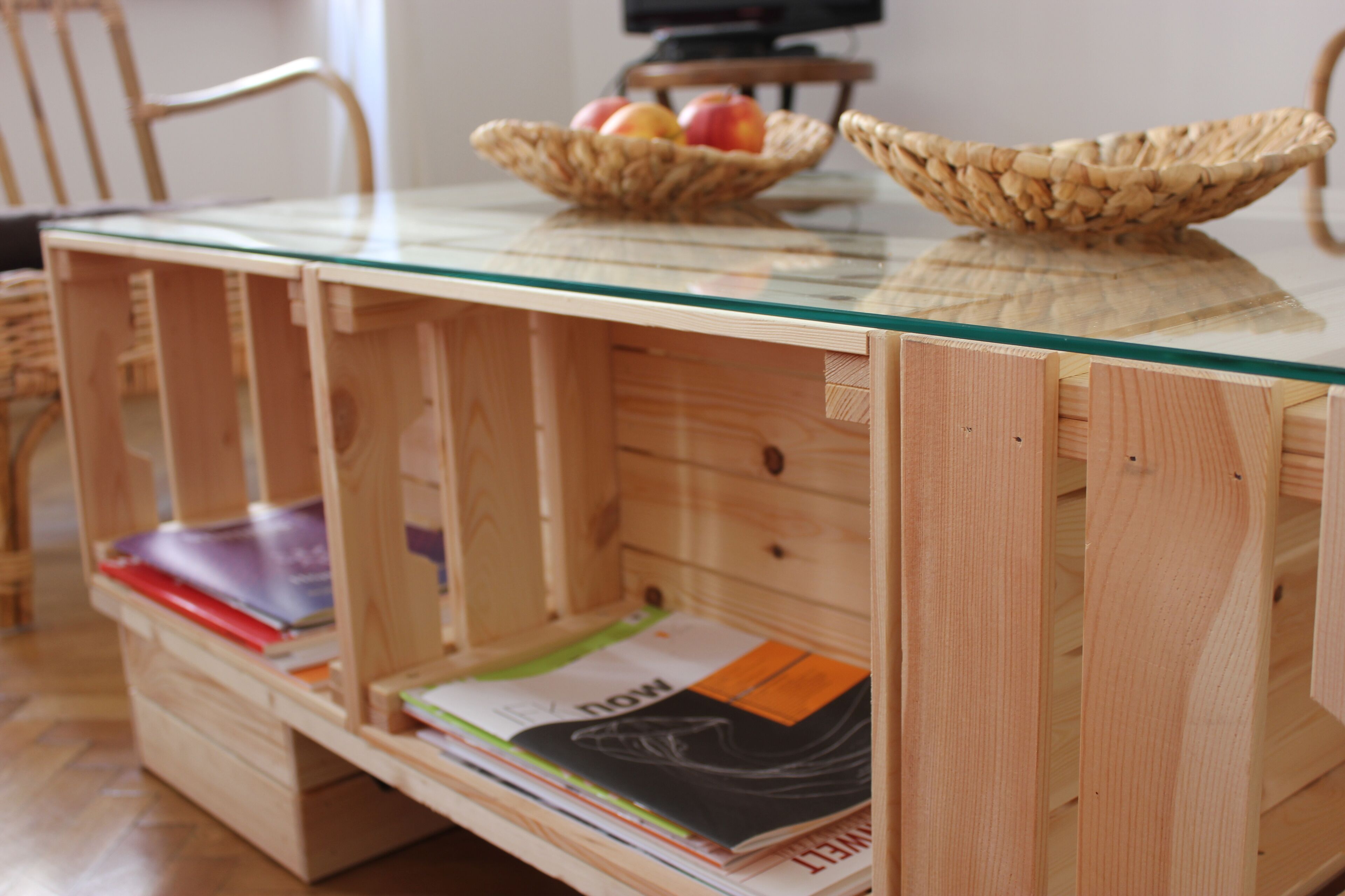 Een houten tafel met glazen blad en twee gevlochten manden vol appels.