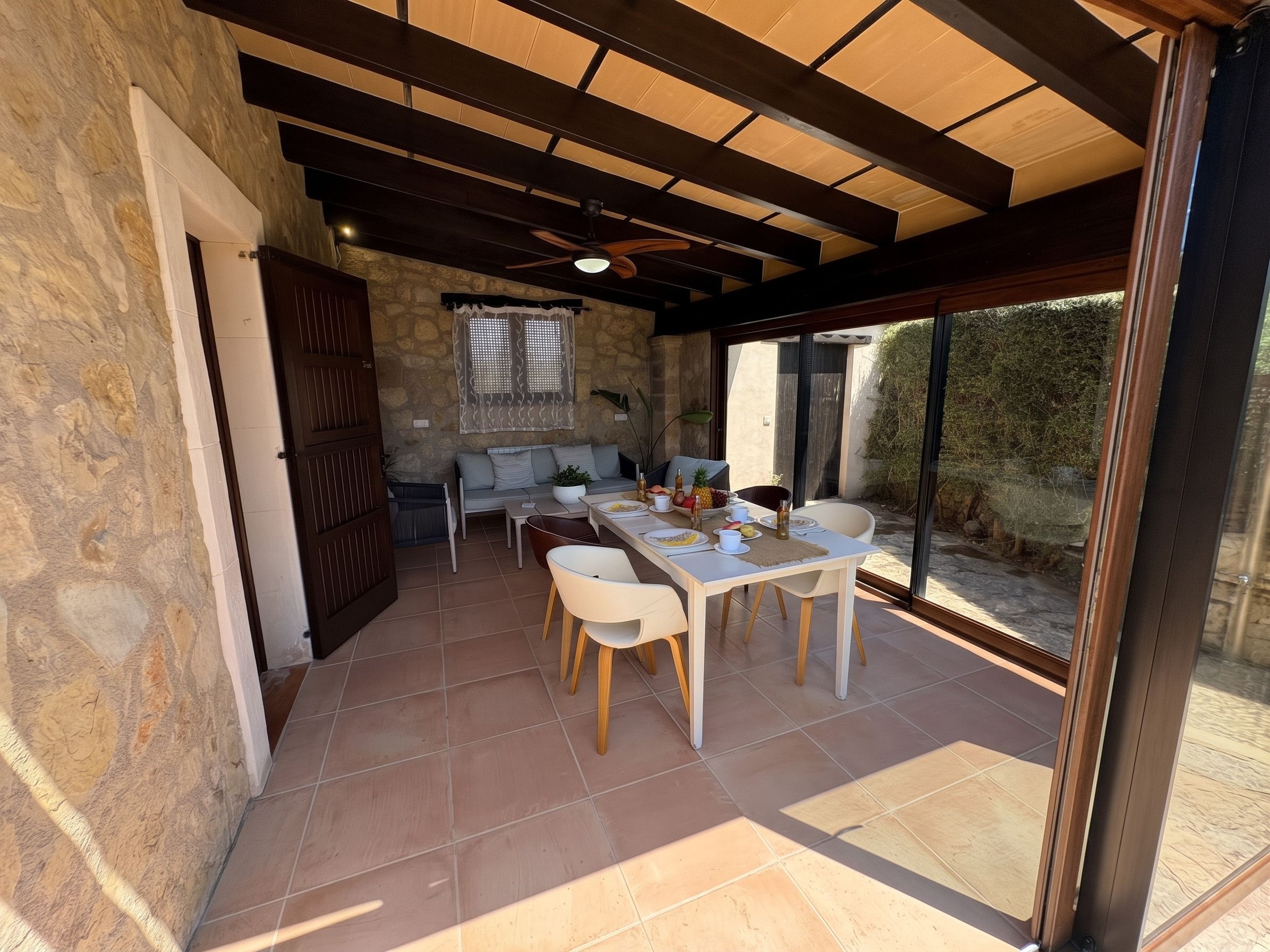 A dining area with a table and chairs, a stone wall, and a view through large windows.