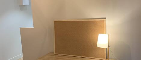 Um espaço de trabalho pequeno e bem organizado, com um quadro de cortiça, uma luminária de mesa e uma cadeira preta.