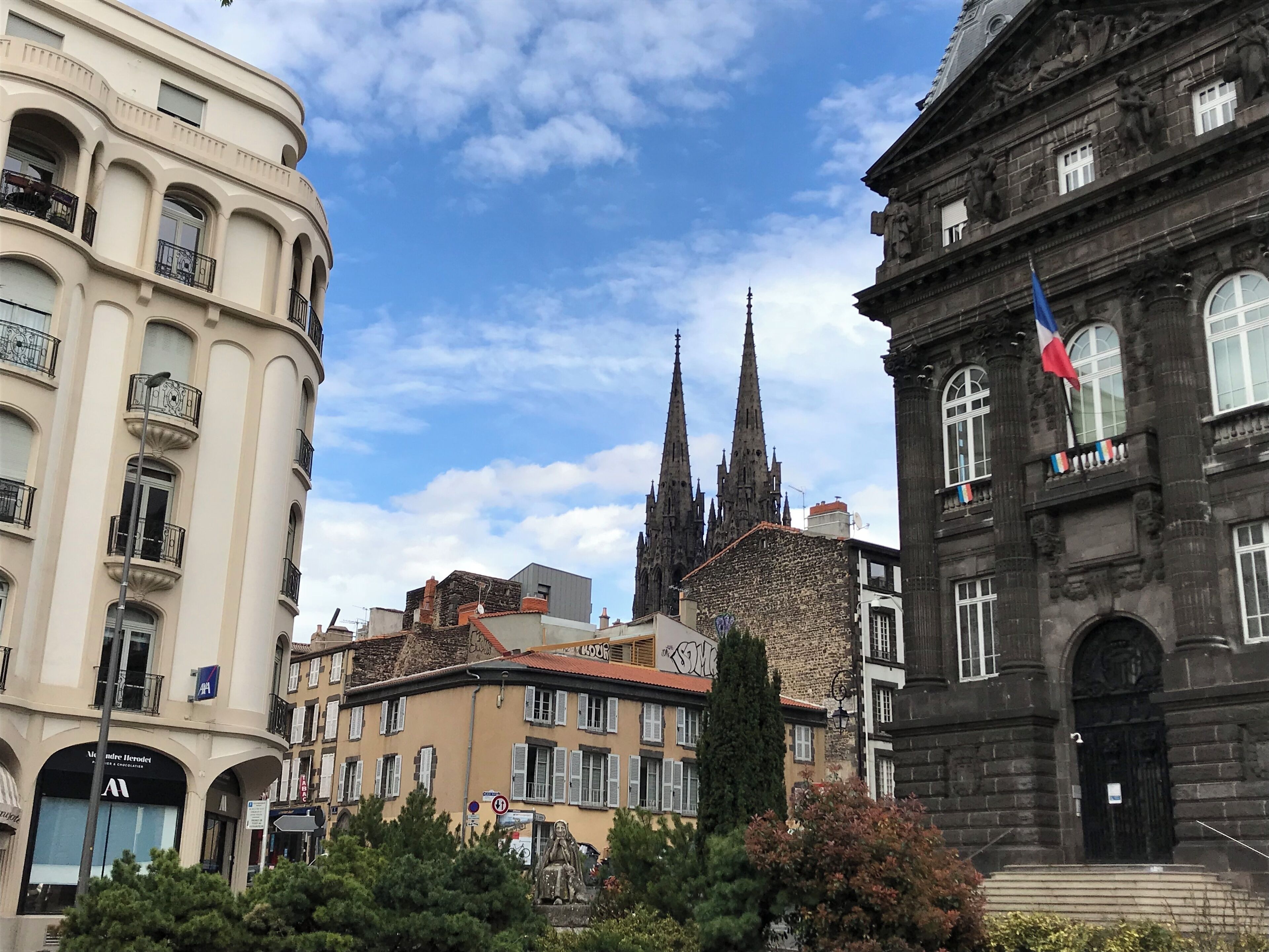 Ein historisches Gebäude mit gotischen Türmen, einer Flagge und einer Statue davor.