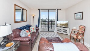 Una sala de estar con un sofá de cuero, una mesa de centro de vidrio, un mueble para la televisión y un balcón con vistas a la ciudad.