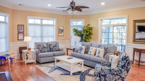 A living room with two sofas, a coffee table, and a ceiling fan. There are windows with blinds, a plant, and a television on a stand. - Sunset Rentals | Crabline 39 | Dog Friendly (Hilton Head Island)