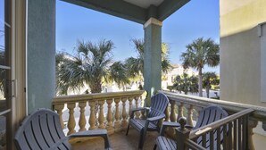 A balcony with a view of palm trees and a building in the background. There are four chairs and a table on the balcony. - Sunset Rentals | Crabline 39 | Dog Friendly (Hilton Head Island)