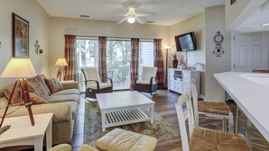 Ein Wohnzimmer mit einer Couch, Sesseln, einem Couchtisch, einem Fernseher und einem Deckenventilator.