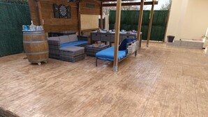 A wooden deck with outdoor furniture, including a sofa and a table, and a barrel. - 4-STAR VILLA TORREILLES SEASIDE RESORT (TORREILLES)