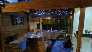 A rustic outdoor seating area with wooden furniture, a bar counter, and string lights. - 4-STAR VILLA TORREILLES SEASIDE RESORT (TORREILLES)