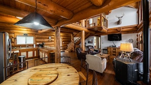 A log cabin interior with a dining area, kitchen, living room, and a mounted deer head on the wall. - Perfect for Families! Big Patio, Pool/Hot Tub (Burnet)