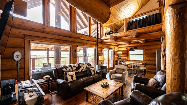 A log cabin interior with a wooden floor, leather furniture, a fireplace, and large windows. - Perfect for Families! Big Patio, Pool/Hot Tub (Burnet)