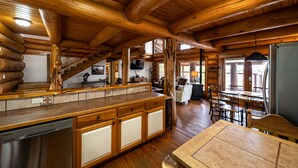 A log cabin interior with a wooden dining area, kitchen counter, and a staircase leading to another level. - Perfect for Families! Big Patio, Pool/Hot Tub (Burnet)