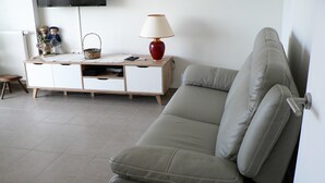Una sala de estar moderna con un sofá gris, una mesita de madera, una lámpara roja y un televisor en la pared.