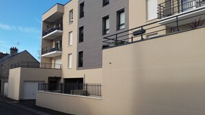 Un moderno edificio residencial de varios pisos con balcones, garaje y entrada protegida por un portón.