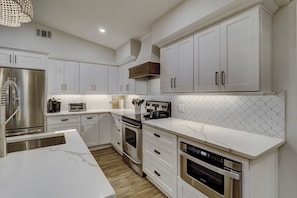 A modern kitchen with white cabinetry, stainless steel appliances, and a marble countertop.