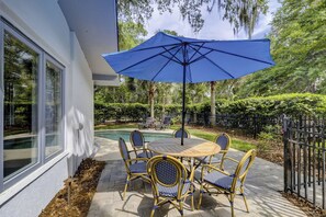 An outdoor patio with a pool, surrounded by a black metal fence, featuring a table and chairs with blue cushions.
