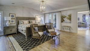 Quarto moderno com cama grande, duas cadeiras, uma mesinha e obras de arte nas paredes.